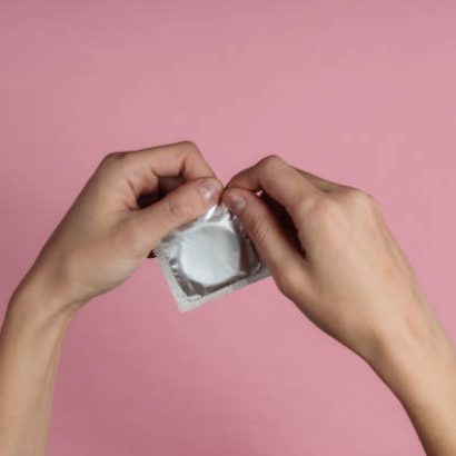 Female hands open a condom on pink background. Top view. The concept of sexual preservation